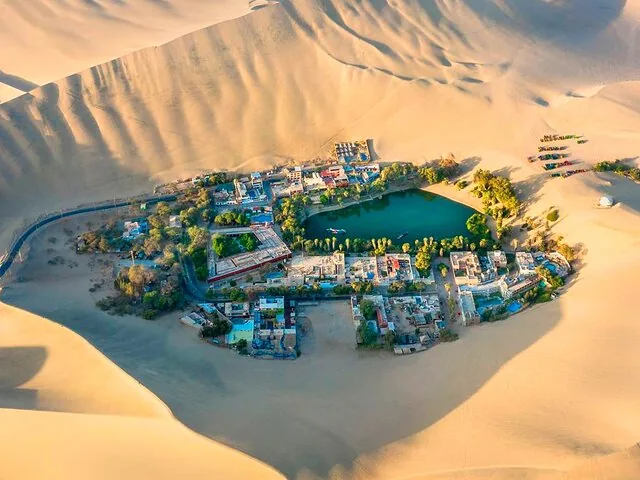 Aerial view of Huacachina Oasis surrounded by massive sand dunes.