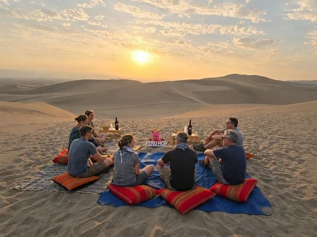 Group of people sitting on a blanket in the desert at sunset.
