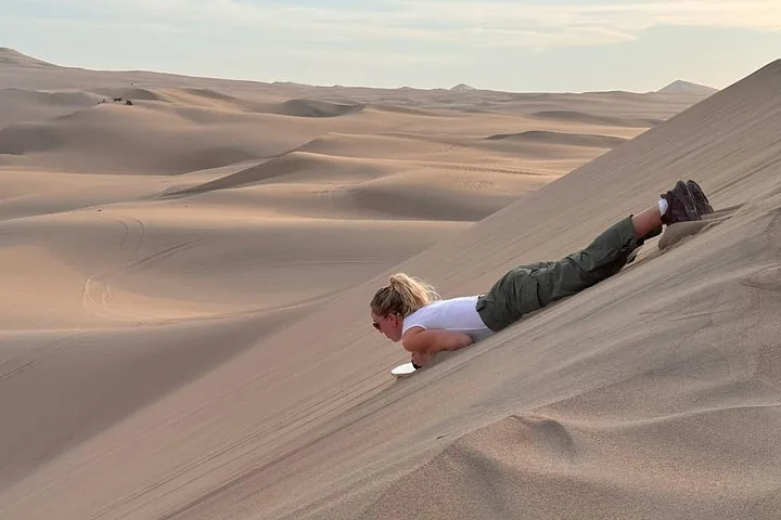 Person sandboarding down a large sand dune in the desert.