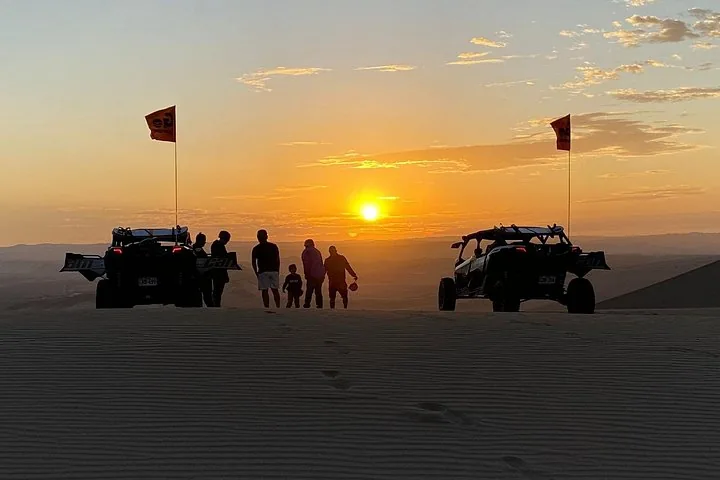 Silhouettes of people and dune buggies in the desert at sunset.