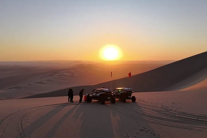 Dune buggies and people in the desert during a bright sunset.
